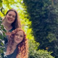 Two alums peek out from behind a tree